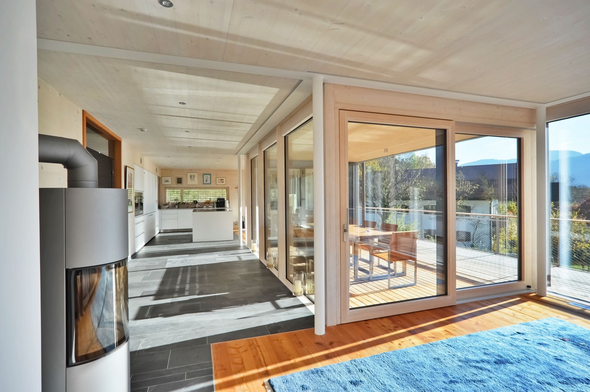 Blick aus einem Wohnzimmer in eine offene, helle Küche mit bodentiefen Fenstern