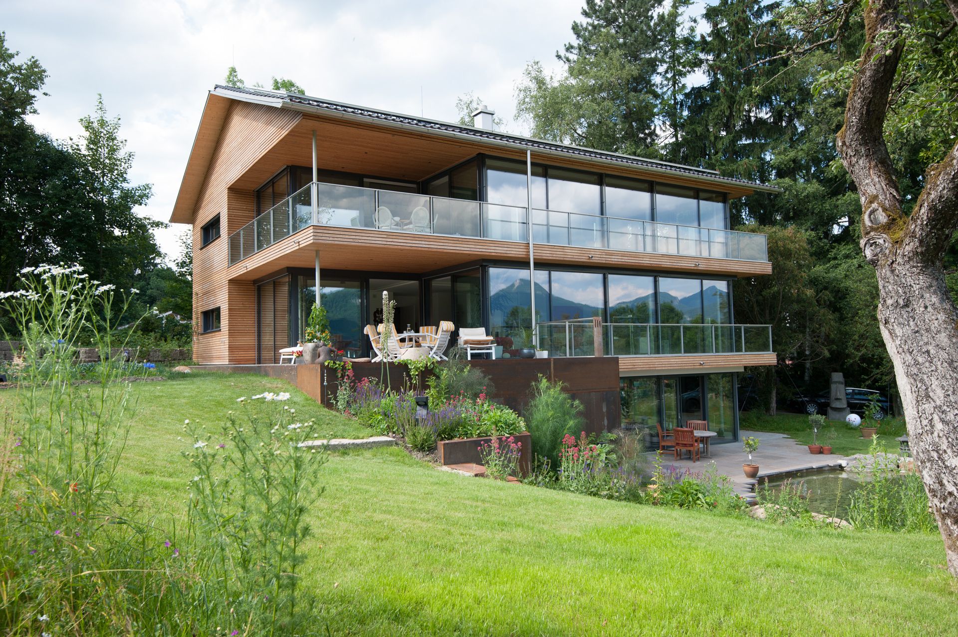 Modernes Wohnhaus mit Holzfassade und großen Glasfronten in Hanglage mit Blick auf die Berge
