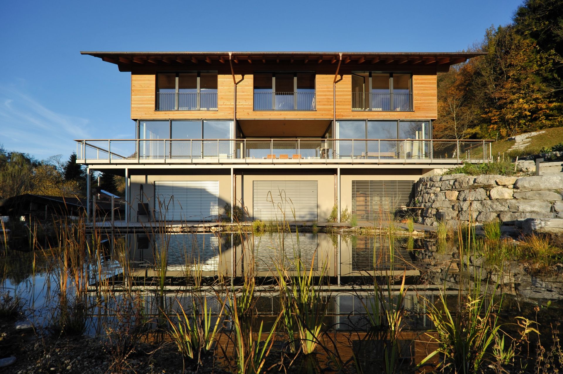 3-stöckiges Wohnhaus mit bodentiefen Glasfronten, Holzverkleidung und angrenzendem, kleinem See mit Schilf